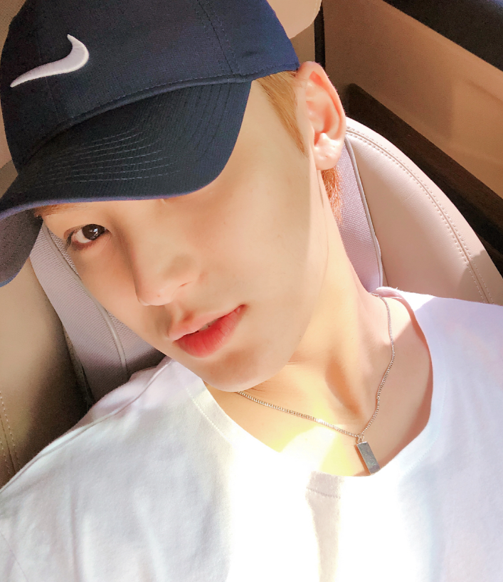 車のシートに座りながら、白いTシャツとシルバーネックレスを身に着けた男性のスタイルが写っている画像。帽子をかぶっています。