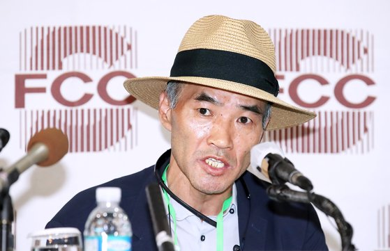 在FCC背景前，一名戴草帽的男子正在記者會上發言，前景有多個麥克風和寶特瓶。