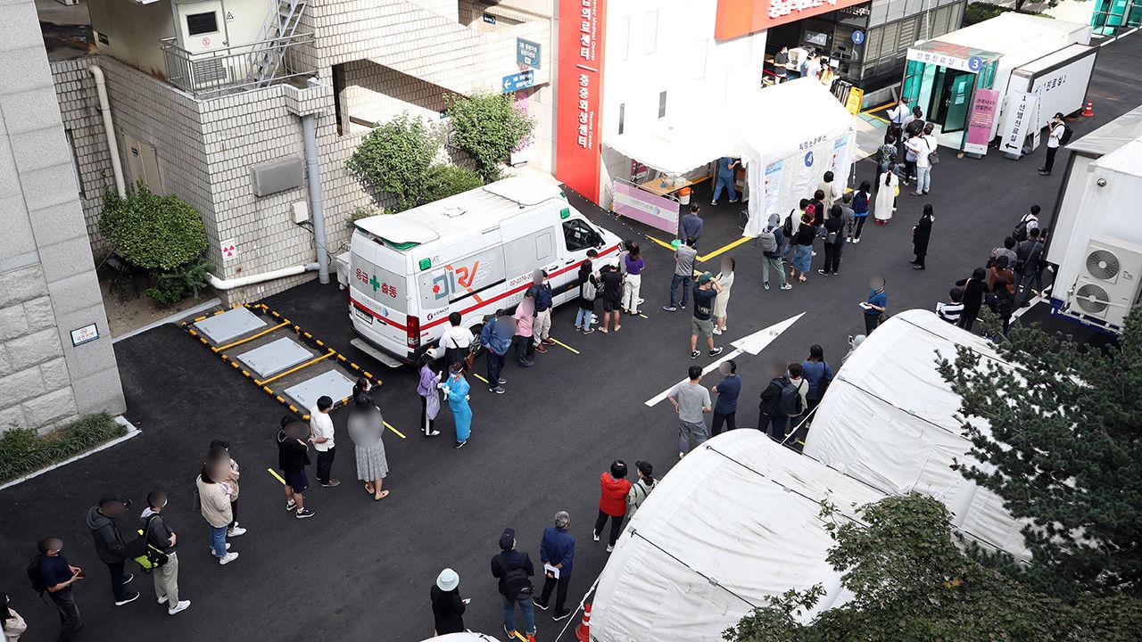 ภาพโควิด-19 เกาหลีใต้: ผู้คนยืนเข้าแถวรอภายนอกศูนย์ตรวจโรค พร้อมรถพยาบาล หน้าหลีกบ้านรูปเขียนเกาหลี