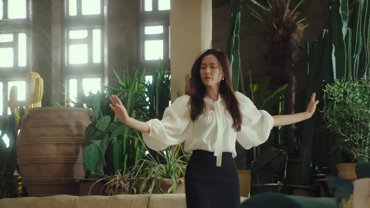 ผู้หญิงยืนอยู่ในเรือนกระจกที่มีต้นไม้สีเขียวล้อมรอบ คาดว่ากำลังเพลิดเพลินกับธรรมชาติ