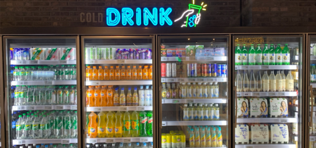 韓國新村 emart 店內的冷藏飲料區，展示了各種瓶裝和罐裝飲品，包括韓國傳統茶與進口果汁。