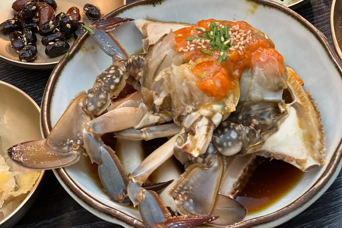 韓國醬油蟹，一隻在醬油中浸泡的生蟹，紅色蟹膏在蟹的殼上閃耀，旁邊配有微辣的泡菜，令人垂涎欲滴，捕捉韓國海鮮的細膩風味。