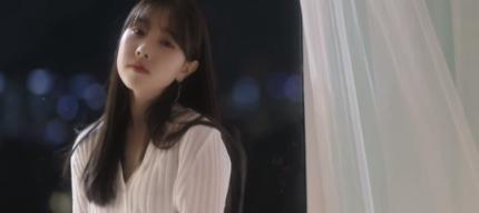 白いシャツを着て夜景を背景に窓辺に立つ女性。