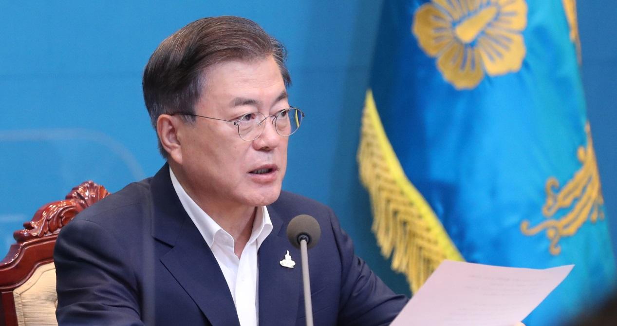 ชายคนหนึ่งในชุดสูทดำกำลังอ่านเอกสารบนโต๊ะที่ประดับด้วยธงชาติ อาจเป็นบรรยากาศการประชุมหรือแถลงข่าว