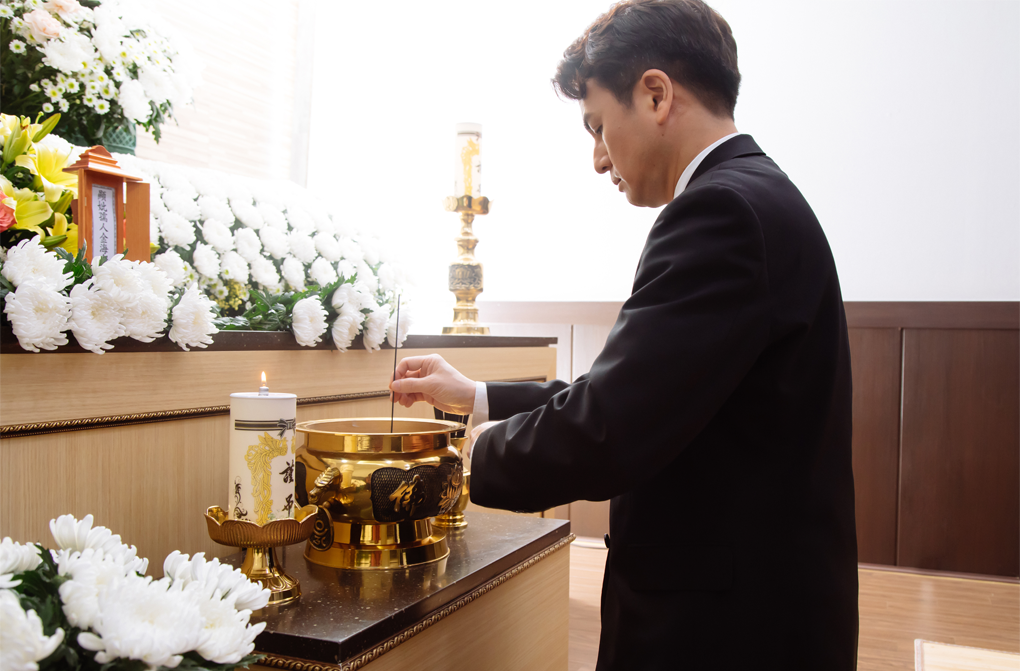 一位身穿黑色正裝的男性在火化室內進行焚香儀式,這是韓國喪禮中的重要敬禮習俗。