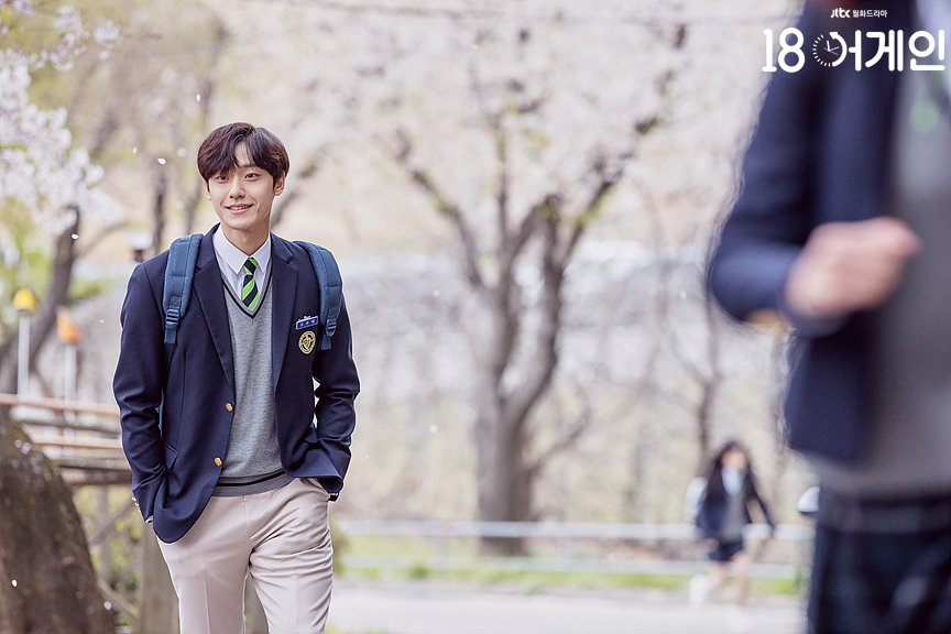 《重返18岁》场景,背景为校园,身穿校服的男演员走在道路上,呈现青春校园的氛围。