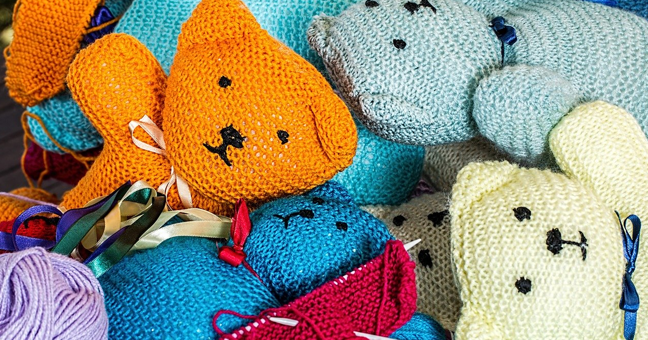 多隻色彩繽紛的毛線玩具熊，堆疊在一起，綁著多種顏色的緞帶