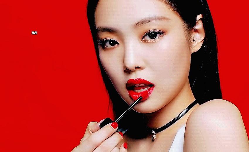 ผู้หญิงถือเครื่องสำอางกับพื้นหลังสีแดง มือถือแปรงทาปาก ที่ทาด้วยเล็บสีแดง