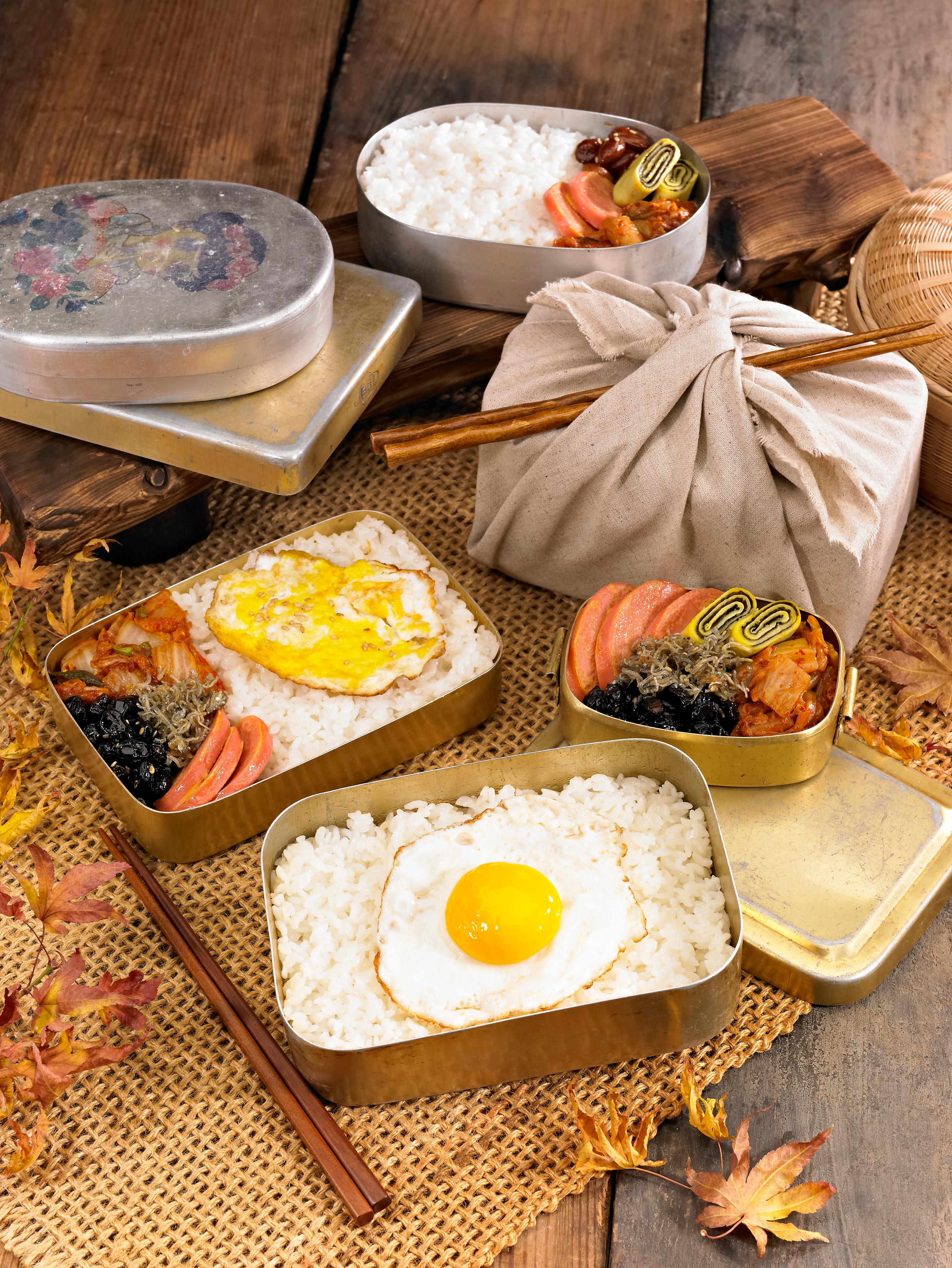 韓国の伝統的なスタイルで包まれた弁当箱。卵やキムチ、海苔が詰まった美味しそうな内容の弁当が木の板の上に置かれている。