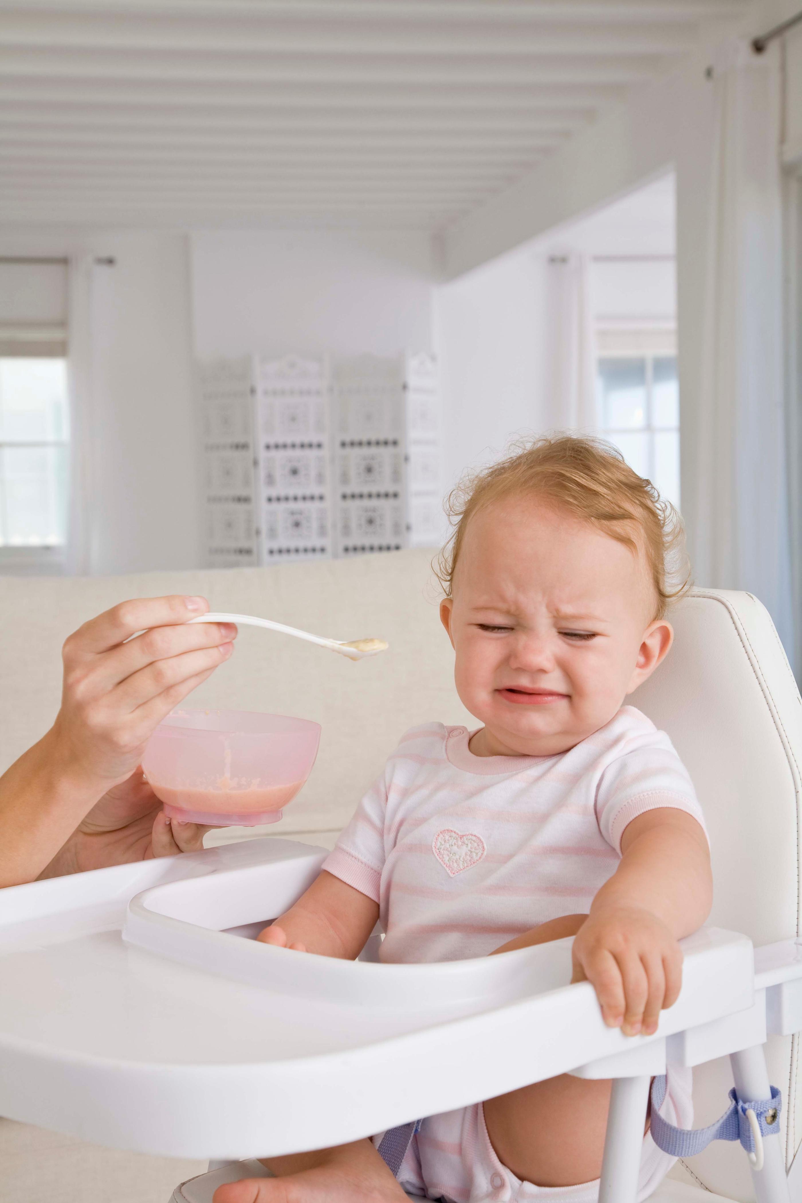 親が赤ちゃんに離乳食をスプーンで与えている様子。家の中でリラックスした雰囲気の中、優しく食事を進める姿が見られる。