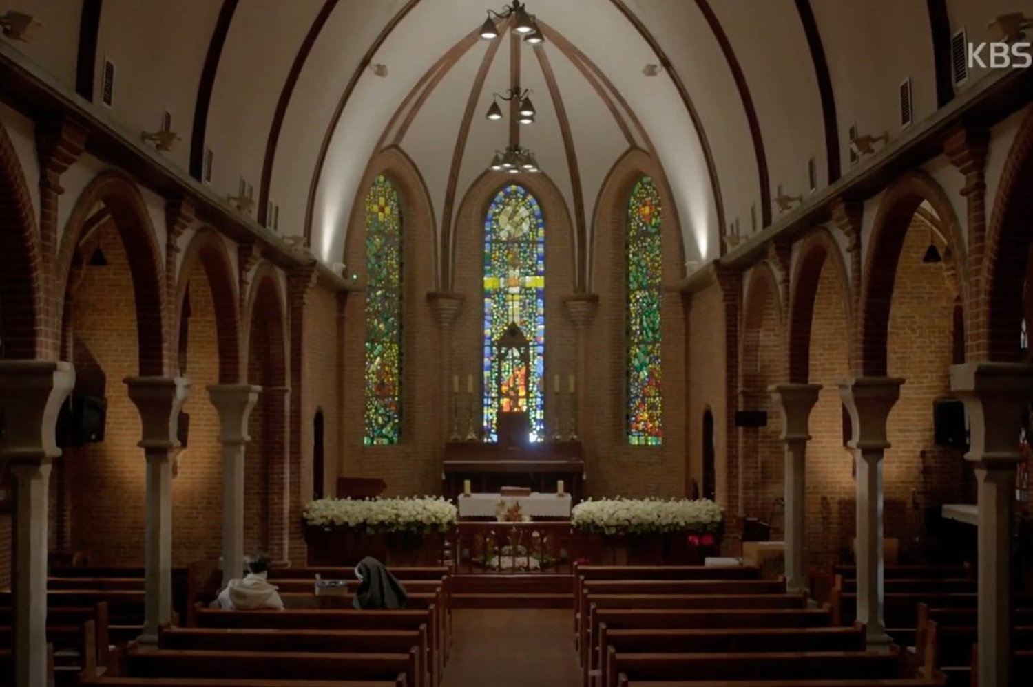 一座教堂內部，拱頂與彩色玻璃窗形成奇幻的光影效果，前景是幾排空無一人的長椅