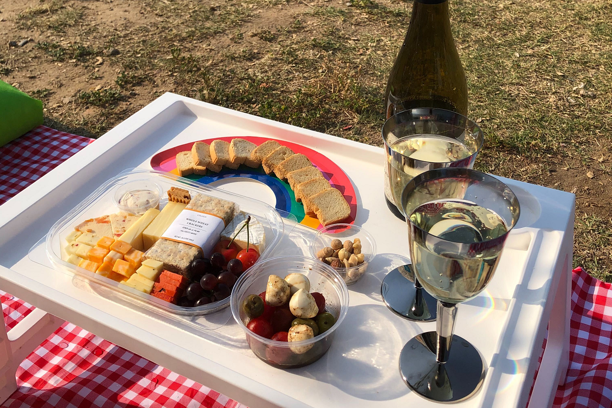 屋外のピクニックテーブルに用意されたワインとチーズ、果物のセット。