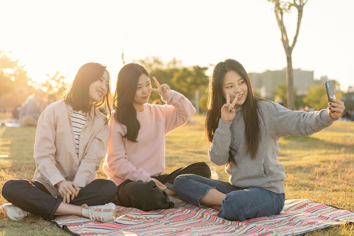 夕方の公園で楽しげに自撮りをする3人の友達。