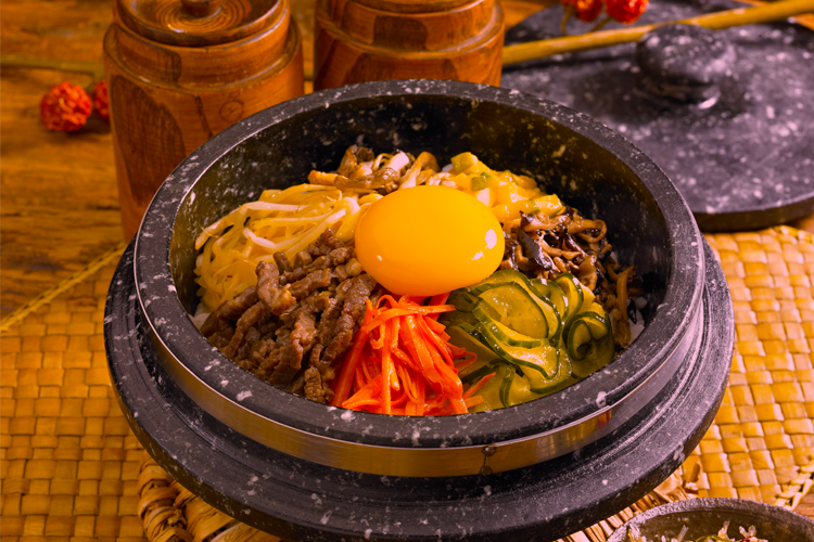 韓式拌飯圖，呈現一碗豐富的韓式拌飯，配有各色蔬菜、蛋黃與芝麻油，滋味細膩。