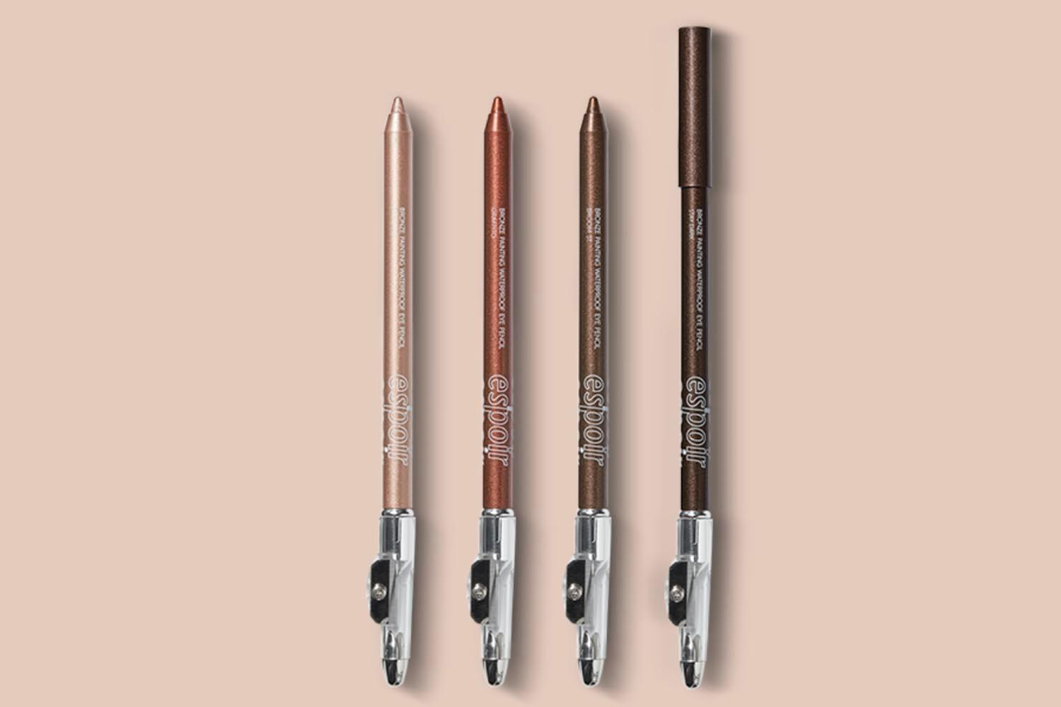 Vier verschiedene Farbtöne des eSpoir Bronze Malstift Eyeliners, die die einzigartigen Nuancen dieser Eyeliner zeigen, auf einem blassrosa Hintergrund fotografiert.