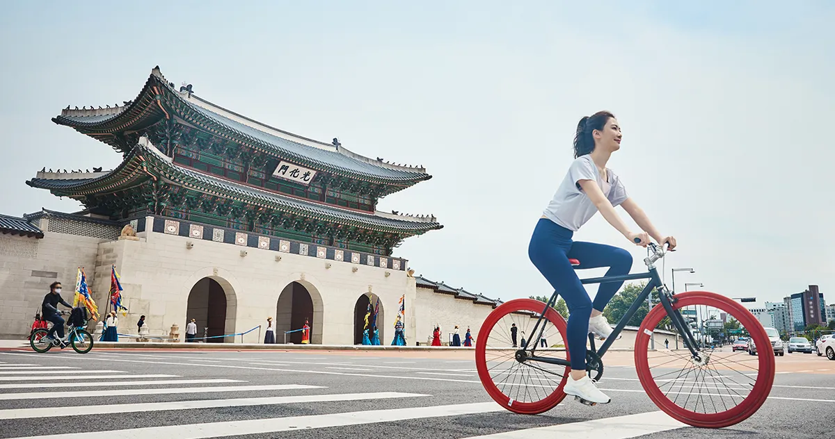 จัตุรัสควังฮวามุนในกรุงโซล ประเทศเกาหลีใต้ มองเห็นหญิงสาวกำลังขี่จักรยานผ่านจัตุรัสและพระราชวังคยองบกกุงเป็นฉากหลัง