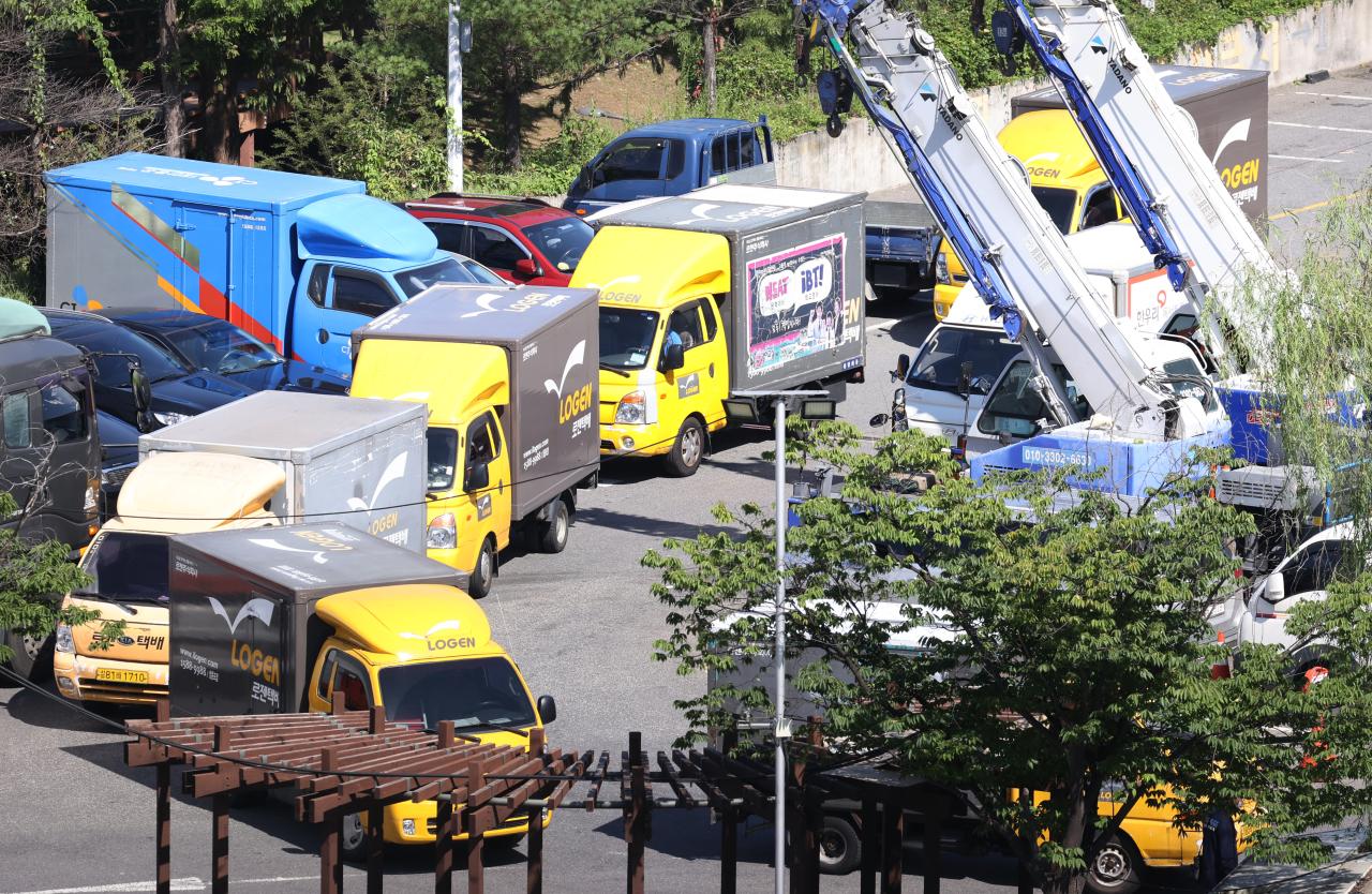 ภาพรถส่งของหลายคันจอดอยู่ในที่จอดรถในเกาหลี สะท้อนถึงความเข้มข้นของงานส่งพัสดุ ซึ่งเป็นสาเหตุหนึ่งของการเสียชีวิตของพนักงานส่งของจากการทำงานหนักจนเกินไป.