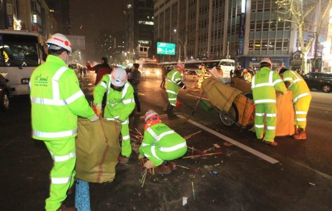 พนักงานเก็บขยะในเกาหลีใส่ชุดสะท้อนแสงสีเขียวอ่อนกำลังทำงานบนถนนกลางคืนในเกาหลี