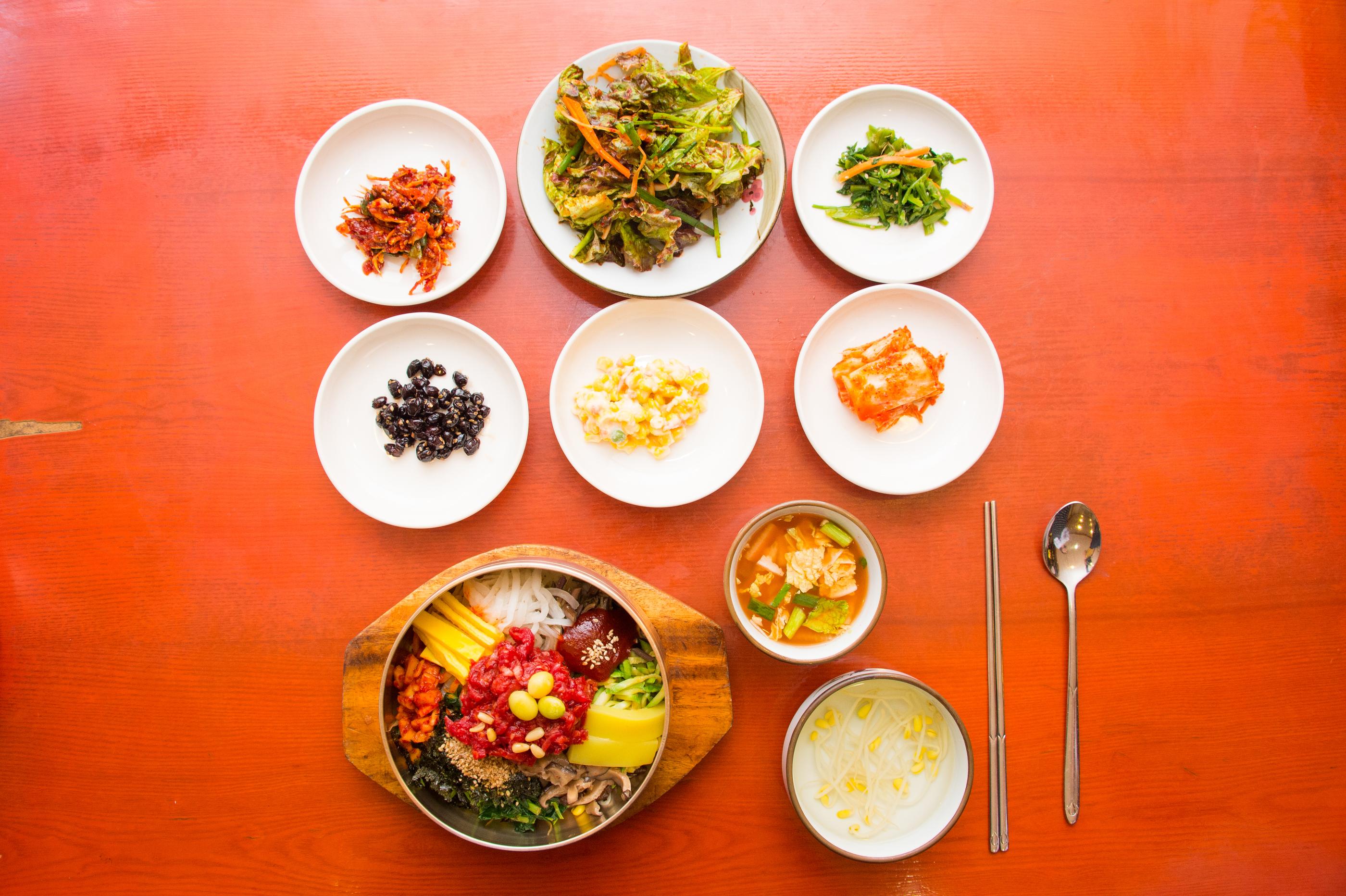 複数の料理が載っている韓国の伝統的な食卓。中心にはユッケビビンバがあり、周囲には様々な副菜が並べられている。