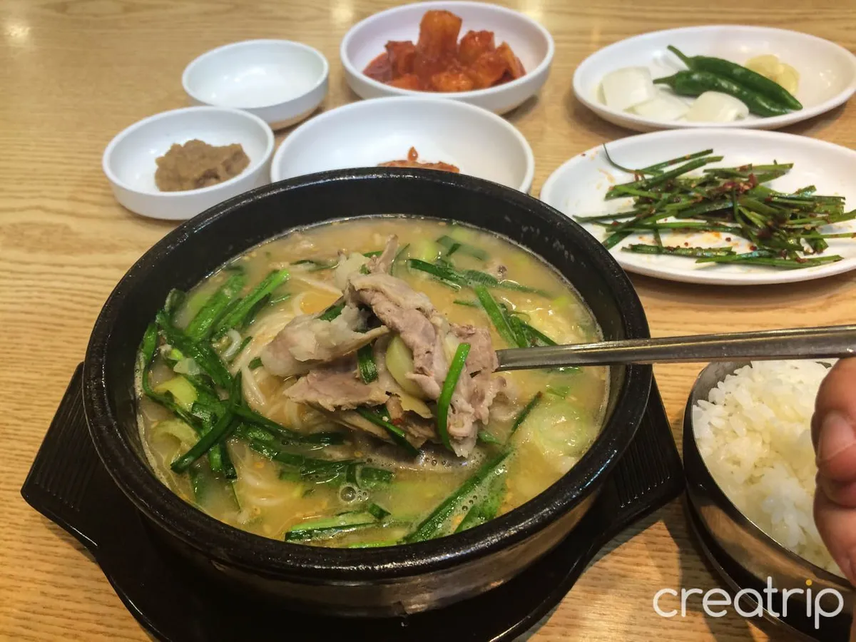 精緻擺盤的韓國豬肉湯飯，全套餐具和鮮嫩的豬肉片，再加上旁邊的泡菜，構成完美的韓國用餐體驗。