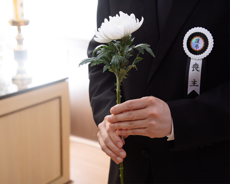 一名穿著西裝的人持著一朵白色菊花，象徵死亡與重生的夢境。