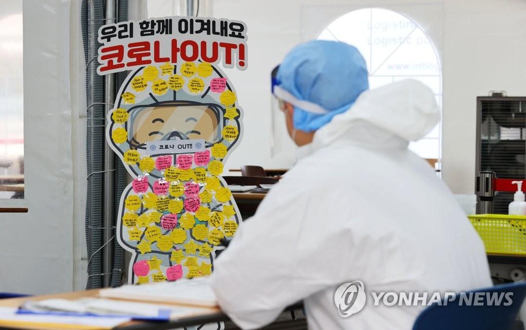 พื้นที่เตรียมความพร้อมต่อสู้โควิดในเกาหลีใต้ พร้อมป้ายข้อความ '코로나OUT!' มีแพทย์สวมชุดป้องกันเตรียมพร้อมให้บริการ