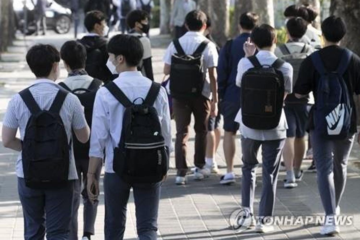 Một nhóm các học sinh mặc đồng phục học sinh Hàn Quốc, đeo ba lô, đi bộ trên một con phố.