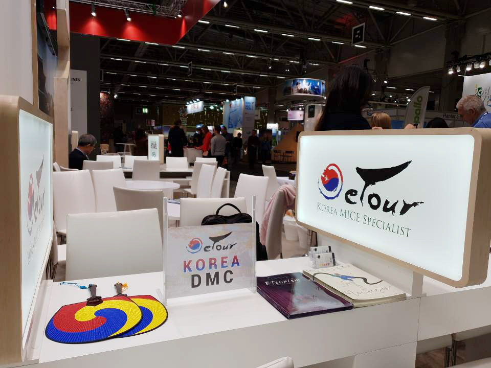 บรรยากาศภายในงานท่องเที่ยวที่จัดขึ้นในเกาหลี มีผู้คนหลากหลายสัญชาติร่วมงานและแสดงภาพสิ่งพิมพ์และโปรโมชันจากศูนย์บริการ MICE ของเกาหลีที่น่าสนใจสำหรับนักเดินทาง