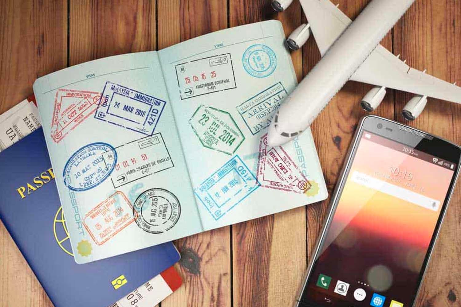หนังสือเดินทางพร้อมวีซ่าและอุปกรณ์การเดินทางบนโต๊ะไม้ แสดงถึงการวางแผนการเดินทางไปต่างประเทศ อยู่บนโต๊ะที่มีเครื่องบินจำลอง โทรศัพท์มือถือบ่งบอกถึงการเตรียมความพร้อมสำหรับการเดินทางอย่างละเอียดถี่ถ้วน