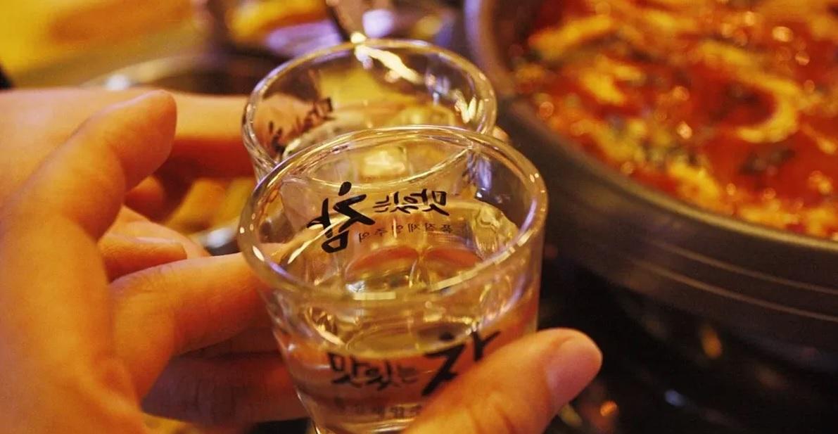 โซจูในแก้วเล็กสีใส พร้อมชามซุปกิมจิร้อน ๆ บนโต๊ะอาหารในบาร์เกาหลี