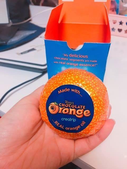 A hand holding a Terry's Chocolate Orange wrapped in its signature orange packaging against a background of a blue box.