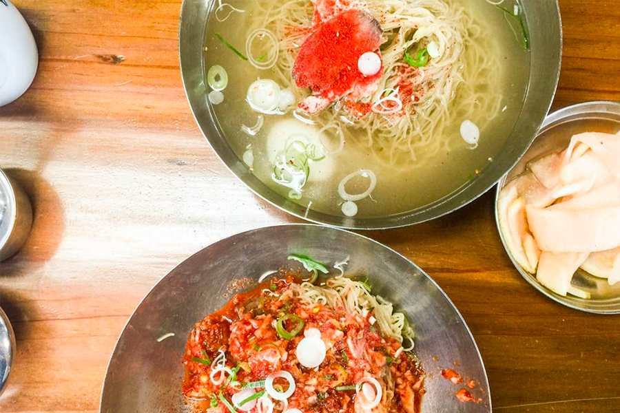 碗裡裝著平壤冷麵的特寫，包含食材、新鮮黃瓜、散發香氣的牛肉清湯，平壤冷麵以厚實的蕎麥麵條為特色。