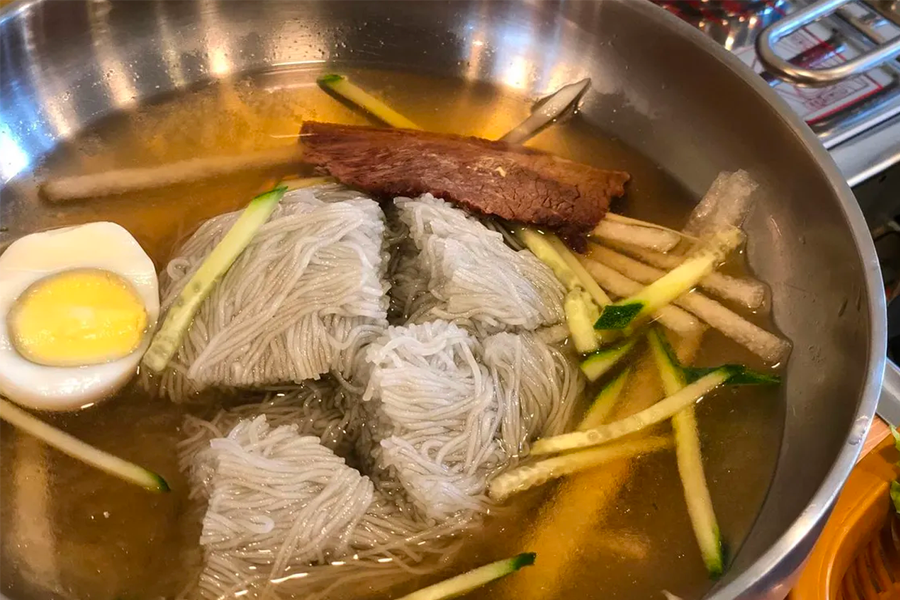 韓國平壤冷麵的特寫，顯示了豐富的配料，如蕎麥麵、湯底、黃瓜、蛋和牛肉切片，美味可口。