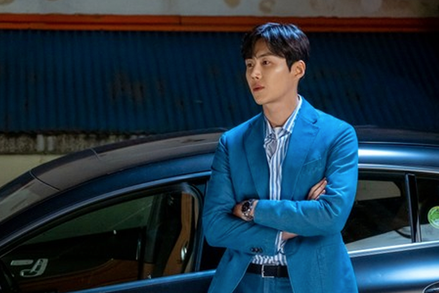 一位穿著藍色西裝的男性站在黑色汽車旁,呈現韓劇《Start Up》中的商業人物形象。