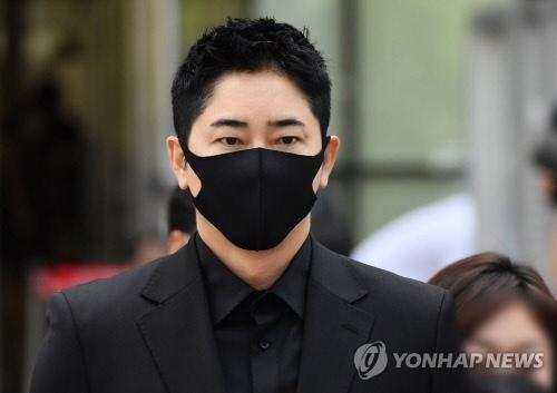 黒いスーツを着た男性が建物の前に立っている、韓国の俳優に関連したニュース記事の一部