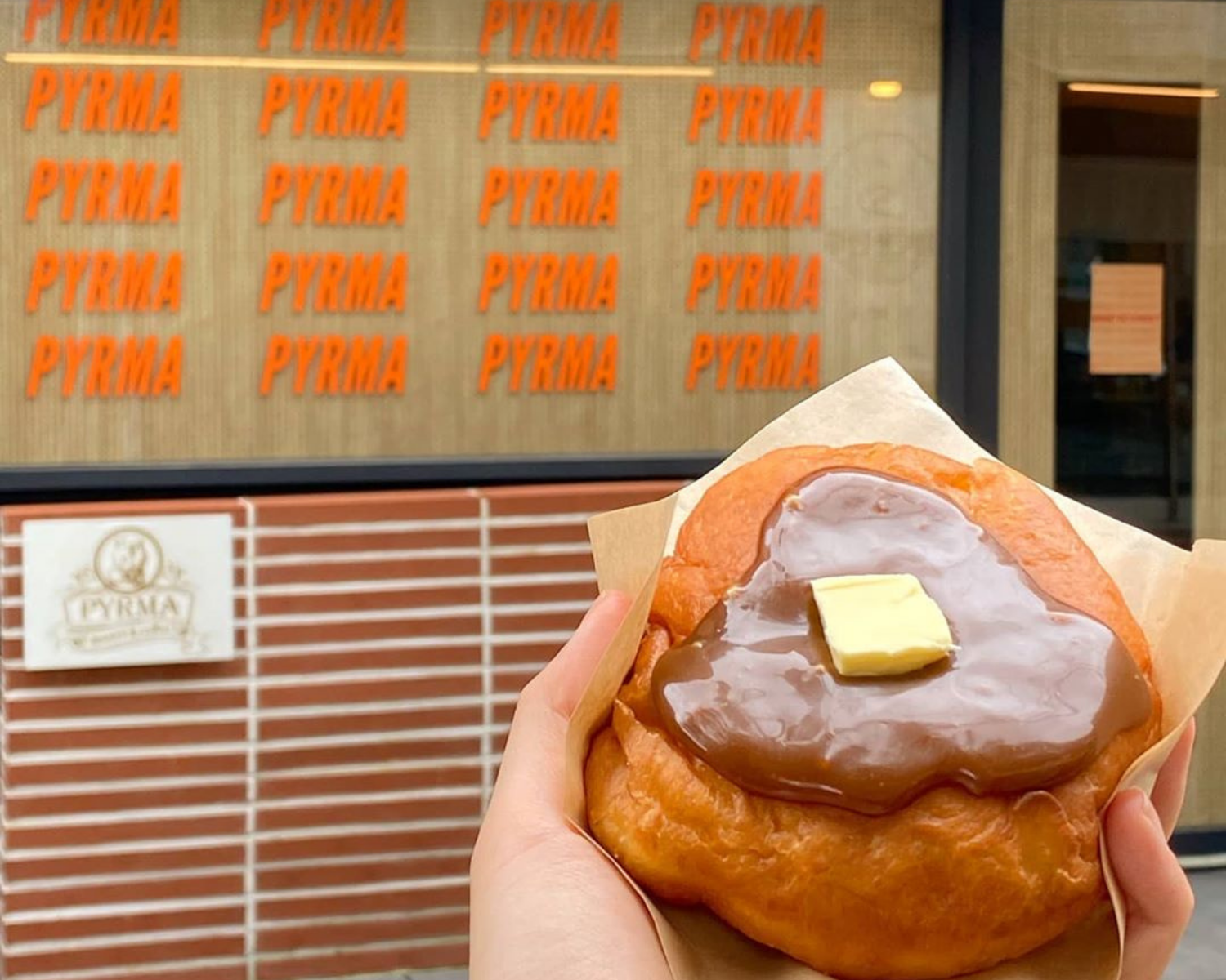 서울 강남에 위치한 피르마(Pyrma) 도넛 카페의 앞에서 카라멜과 버터로 토핑된 도넛을 손에 들고 있는 사진, 독특한 디자인의 한국 도넛 카페