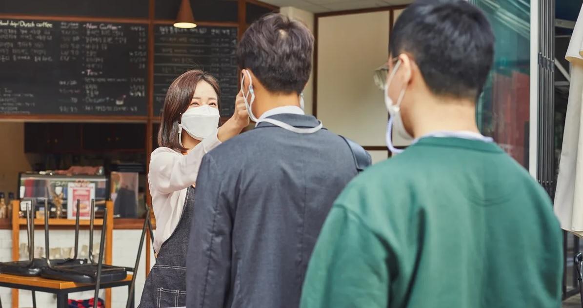 ชายสองคนยืนอยู่ในคาเฟ่โดยมีพนักงานวัดอุณหภูมิด้วยอุปกรณ์ wในขณะที่สวมหน้ากากเพื่อป้องกัน COVID-19