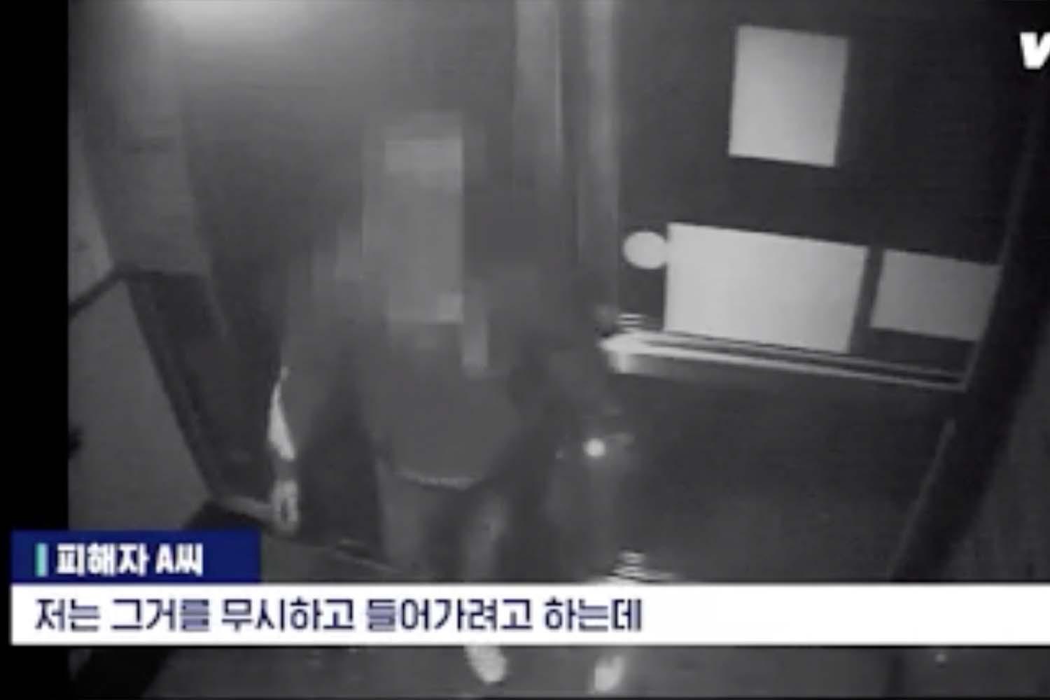 ภาพจากกล้องวงจรปิดในสิ่งแวดล้อมที่มีแสงน้อย แสดงมนุษย์สองคนเดินอยู่ในอาคารที่มีแสงสว่างจากด้านบน ข้อความภาษาเกาหลีกำลังแสดงบนหน้าจอ.