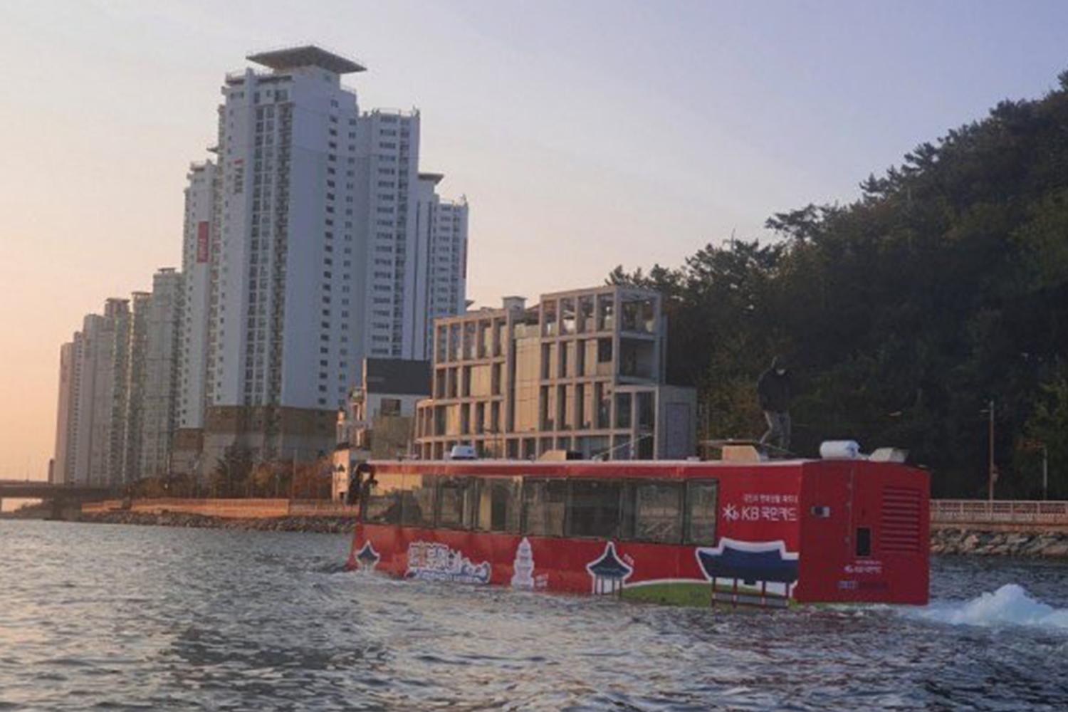 釜山海陸兩用巴士，紅色巴士在水面上行駛，背景是高層建築及海邊景色。
