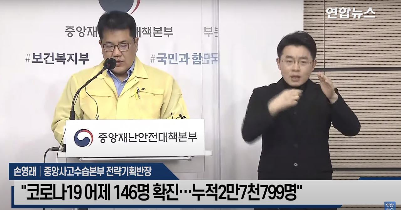 政府官員於COVID-19疫情記者會上發表最新確診統計，旁邊有手語翻譯協助傳遞資訊。