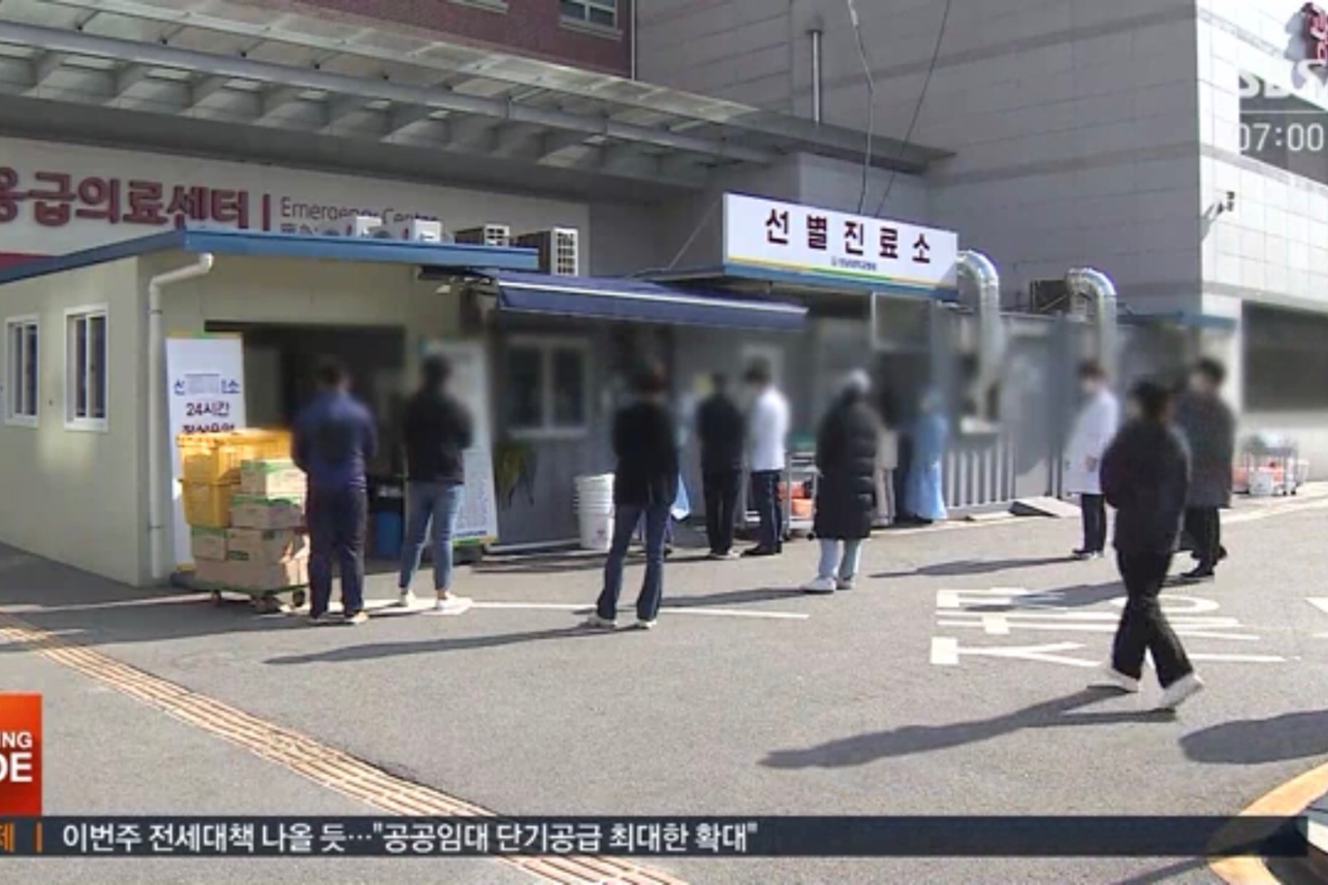 在醫院外，民眾在等待COVID-19檢測，前景可見急診中心和臨時診療所入口。