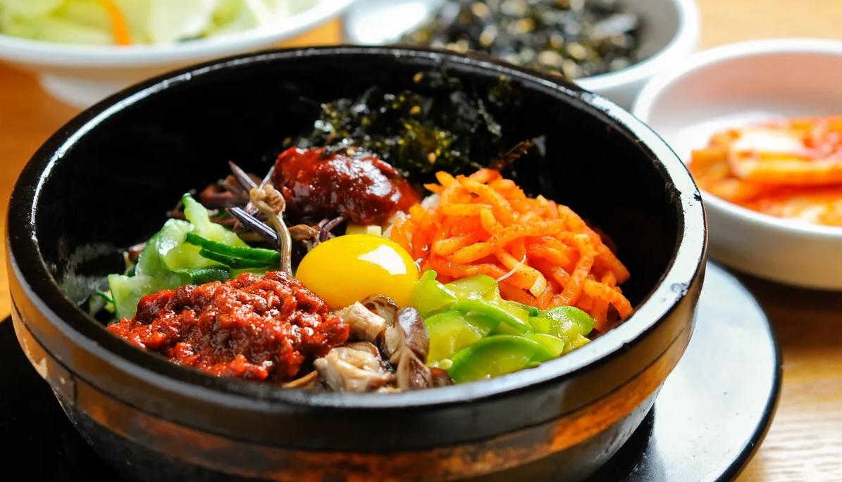 บิมบิบับ เมนูยอดนิยมของอาหารเกาหลีพร้อมผักหลากสีและไข่แดงสดในหม้อดินร้อน จัดเสิร์ฟพร้อมเครื่องเคียงทั้งกิมจิและซุปสาหร่าย ทำให้ดูน่าอร่อยและมีสีสันสดใส