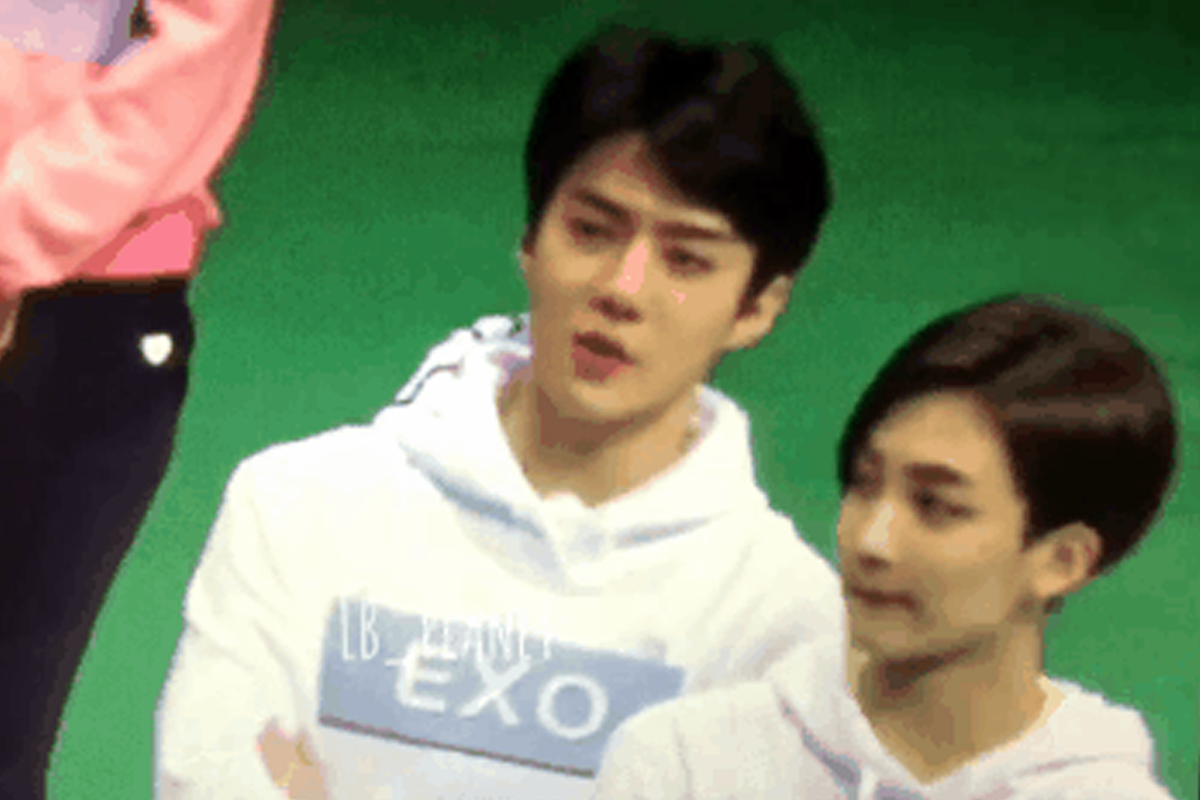 EXO公開活動時於偶像運動會上的爆笑瞬間，背景看似運動場景，其中一名成員穿著白色連帽衫，上面印有EXO字樣，正在活動中進行互動