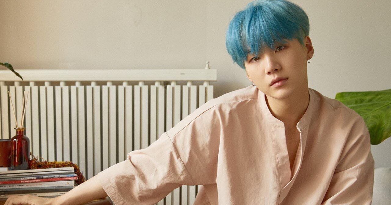 韓國熱門團體BTS的一位成員，特徵是藍色頭髮和在家居中擺姿勢，背景是簡約的室內裝潢