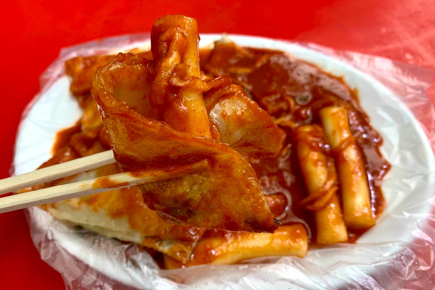 韓国の伝統的なストリートフードであるトッポッキとマンドゥを箸で持ち上げるシーン