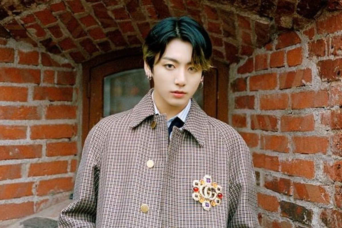 BTS成員柾國身穿白色西裝和稻草帽，背景為新鮮植物牆裝飾。