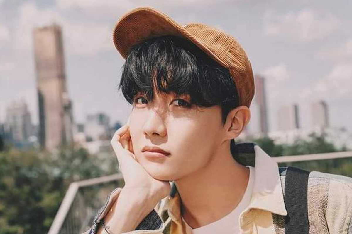 BTS成員J-hope身穿粉色上衣，背景為藍色的大型裝置。