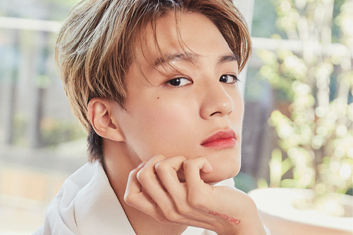 NCT成員Jeno下載陽光照射下坐着的姿態，穿著白色服裝。