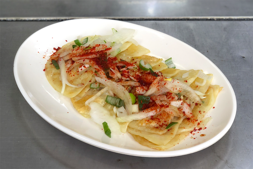 圆盘装的大邱特色薄饺子，上面配有洋葱和辣椒粉，为经典的地道小吃体验。