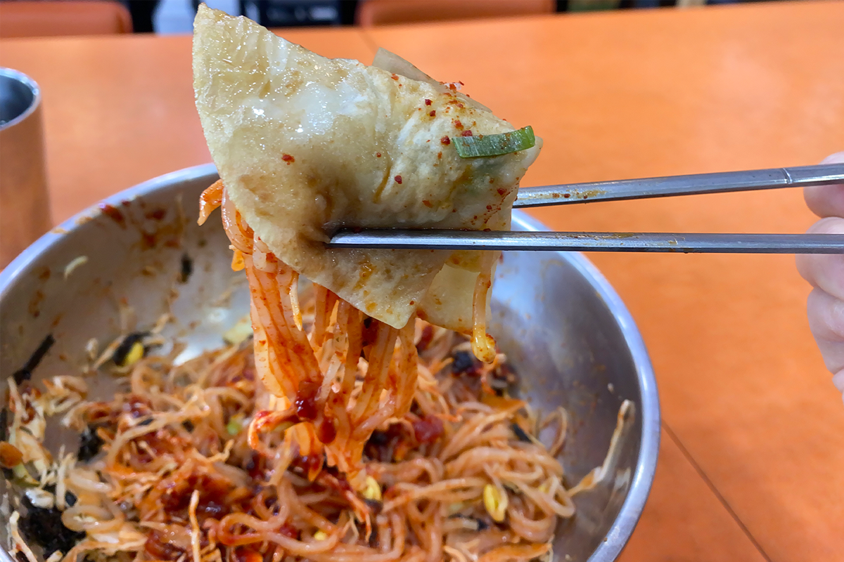 用筷子夹着薄饺子和拌面，展示了这种独特配搭的口感与美味，推荐尝试的美食选择。